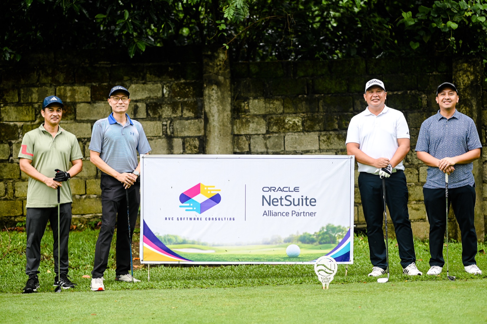 A foursome of golfers posing beside the AVC Software Consulting and Oracle NetSuite tee sign