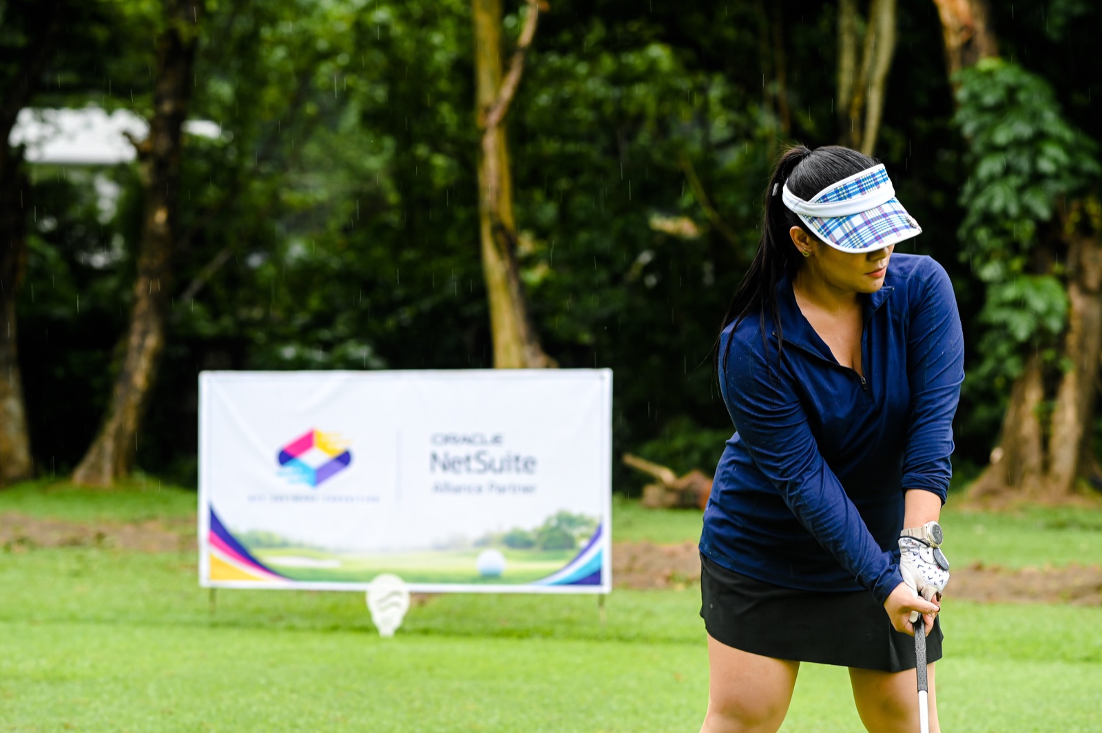 A golfer preparing to tee off beside the AVC Software Consulting and Oracle NetSuite tee sign