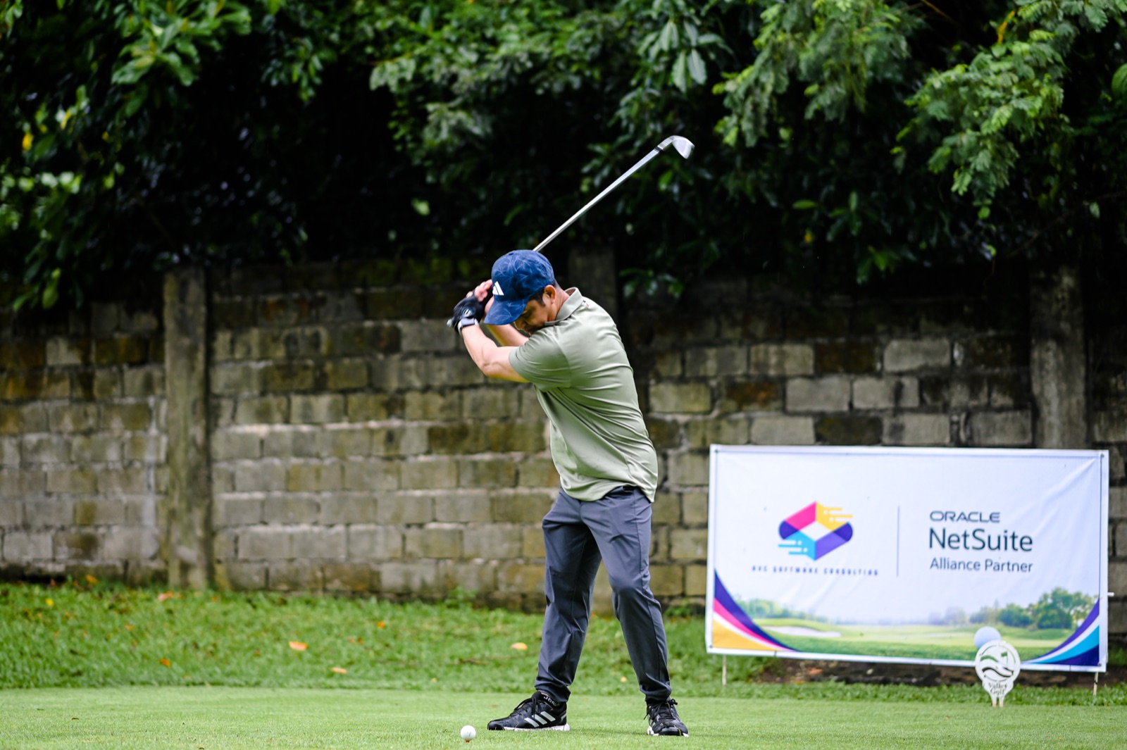 A golfer completing his swing beside the AVC Software Consulting and Oracle NetSuite sponsor banner