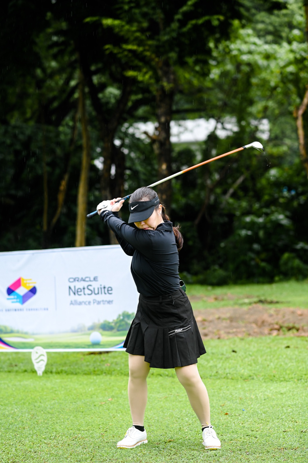 A golfer mid-swing on the fairway in the rain