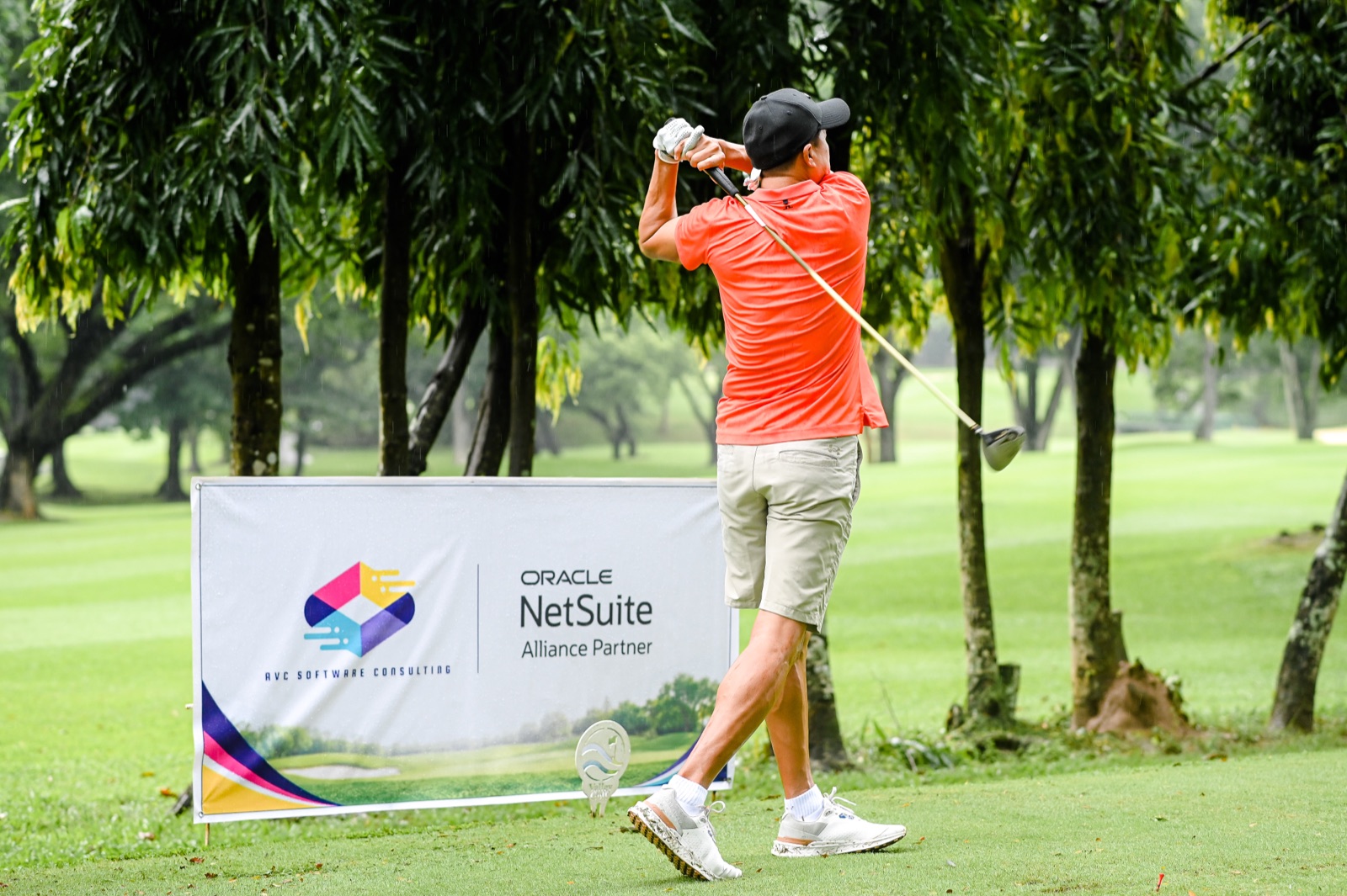 A golfer completing his swing beside the sponsor banner