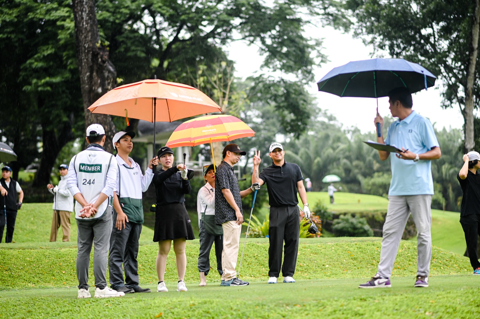 Golfers and caddies gathered under umbrellas discussing play in the rain