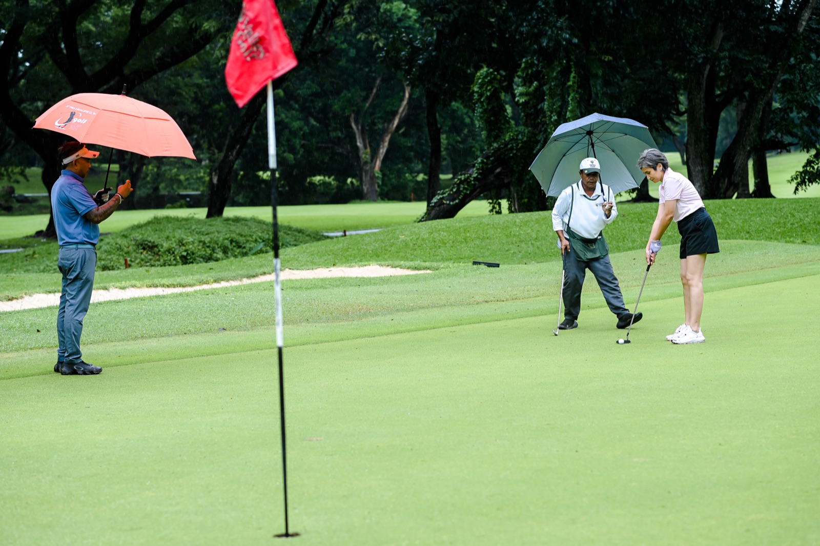 Golfers and caddies on the putting green under umbrellas