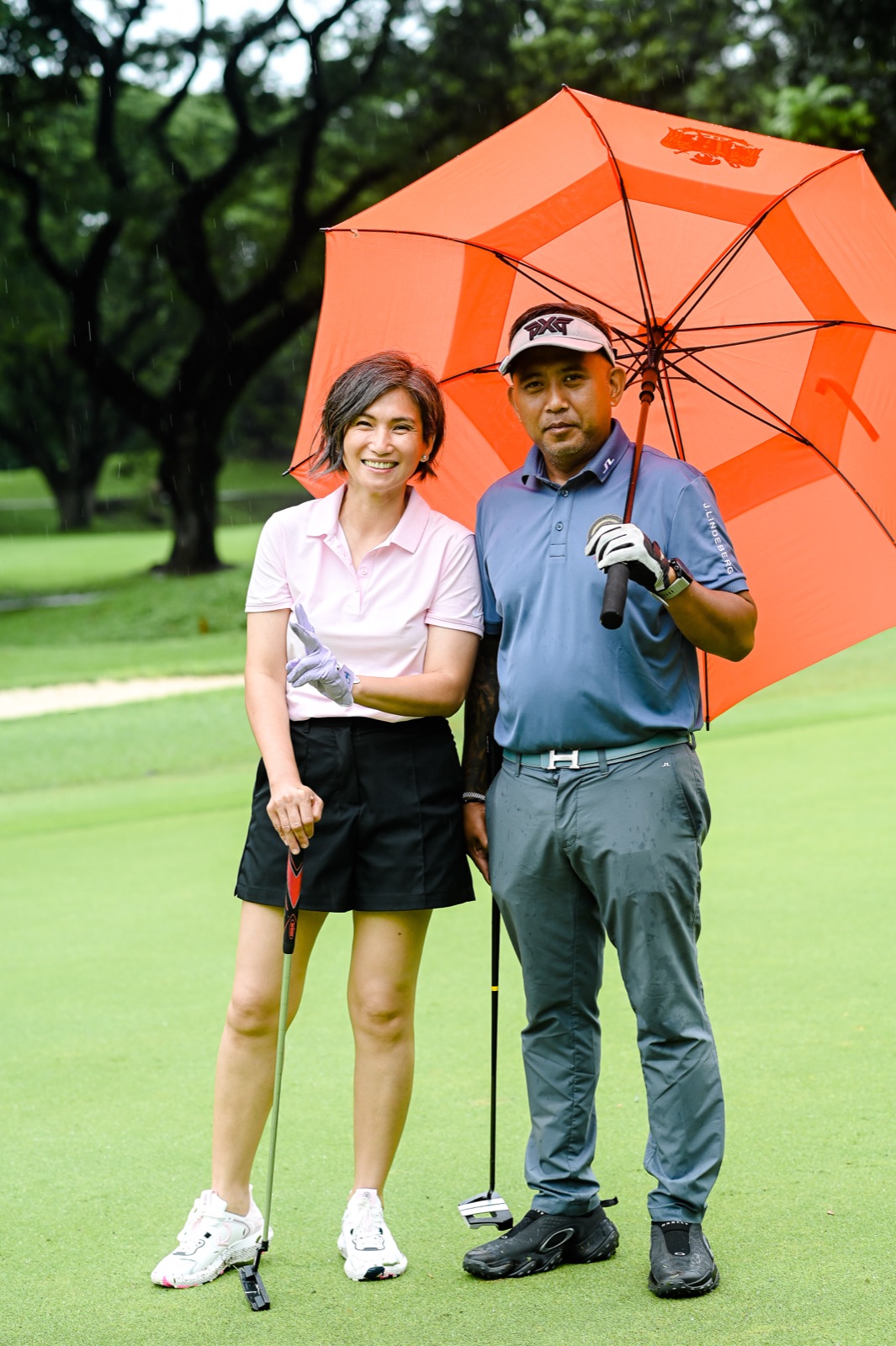 Two golfers sharing an umbrella on the course