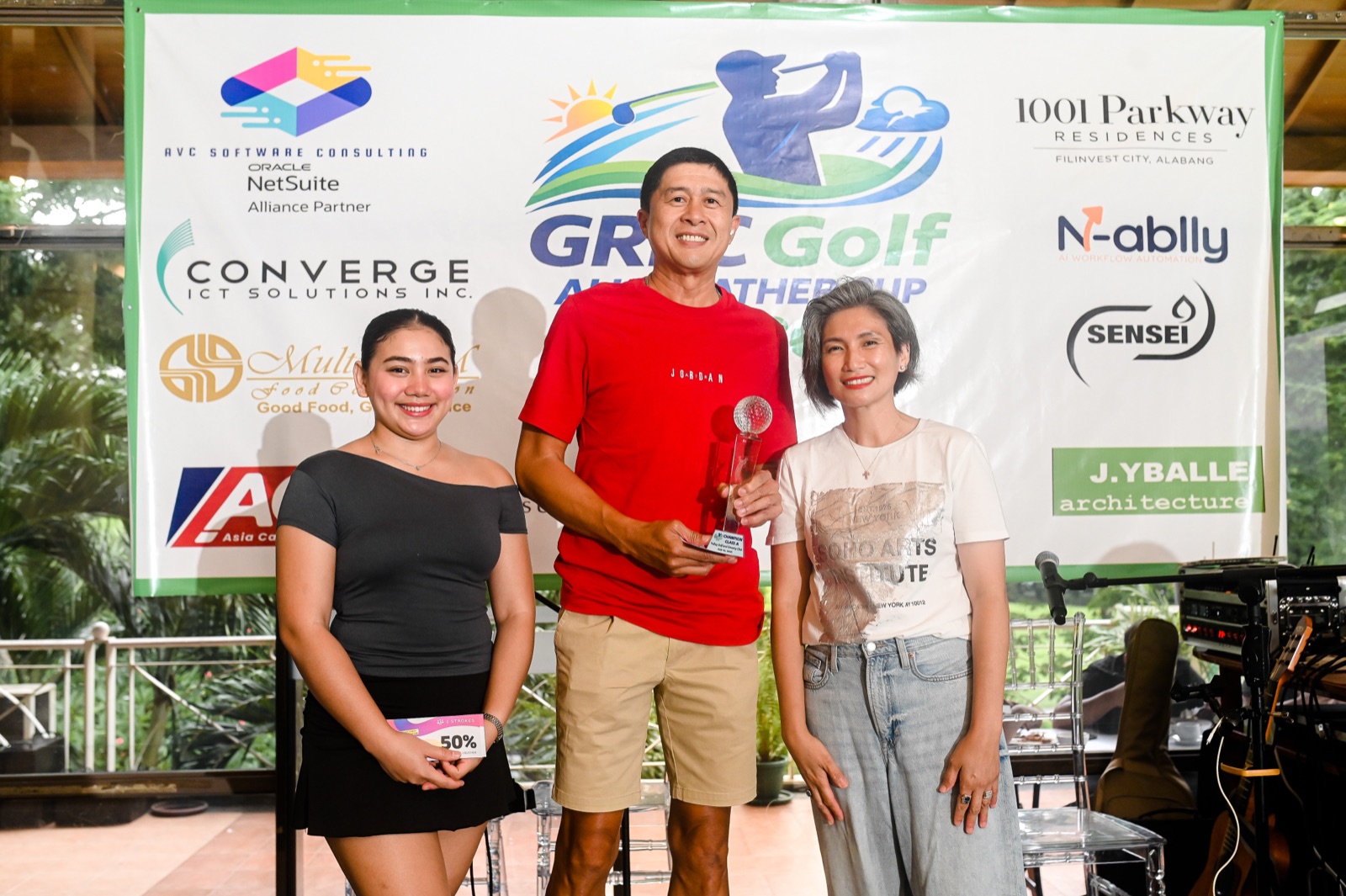 A tournament winner receiving a trophy in front of the GREC Golf All Weather Cup 2026 sponsor backdrop