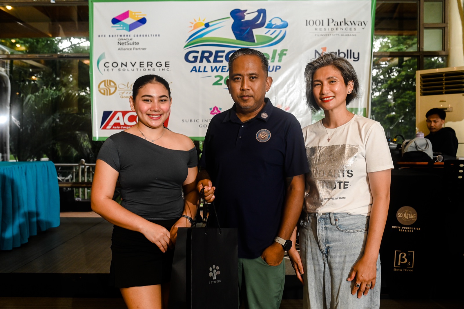A raffle winner receiving a gift bag in front of the GREC Golf All Weather Cup 2026 sponsor backdrop
